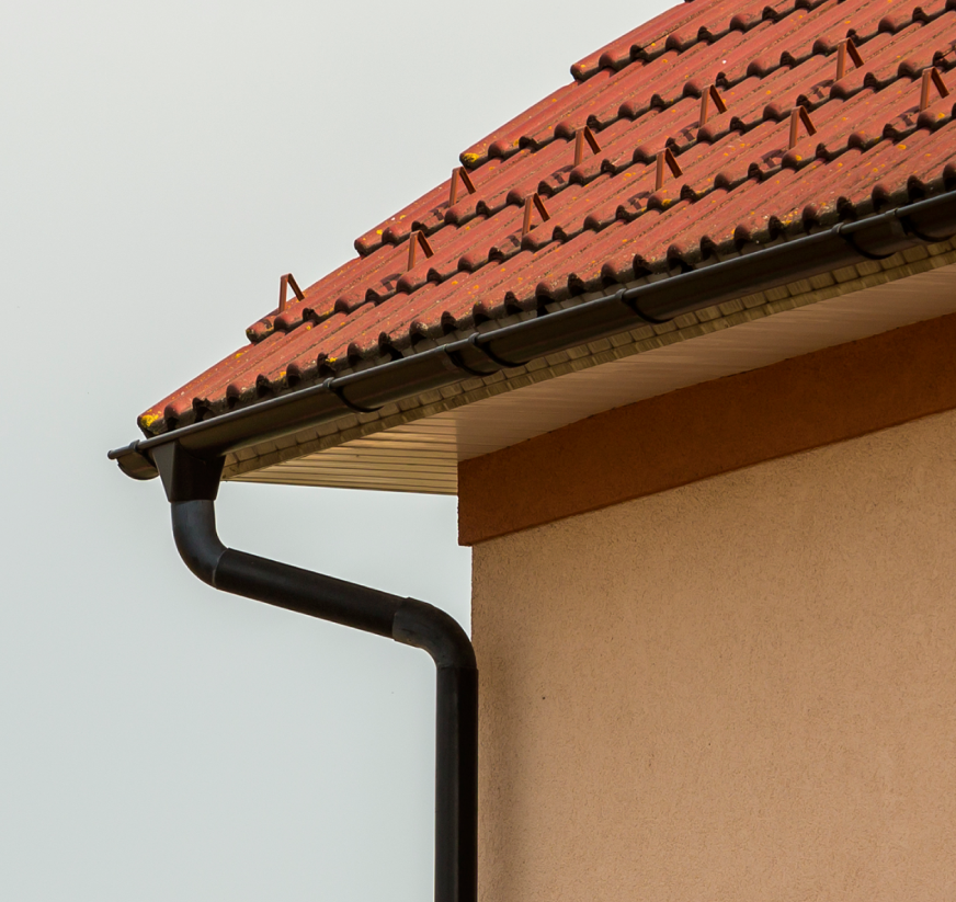 residential roof with clay tiles and seamless gutter system with downspout installed on home exterior