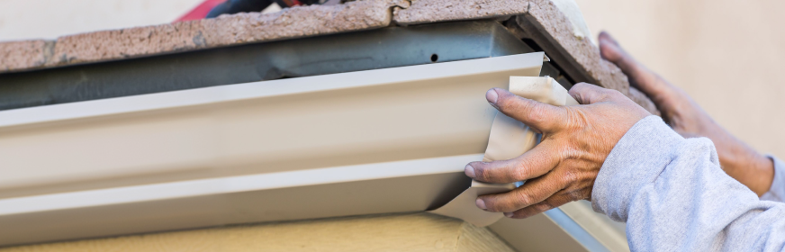 hands adjusting seamless gutter system on house exterior
